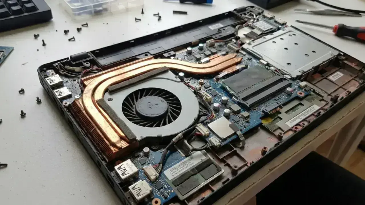 Why is My Laptop Fan So Loud image - a disassembled laptop chassis showing thick dust accumulation blocking the copper heatsink fins and cooling fan blades.